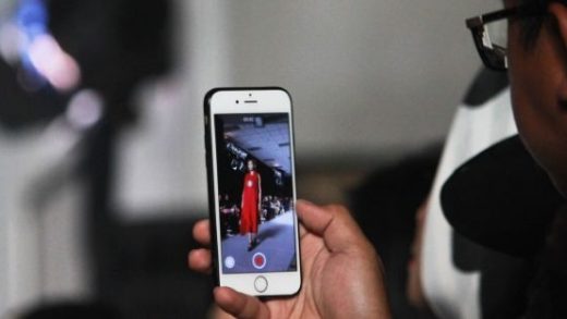 Photograph of person using mobile phone to take a picture of someone modelling clothing