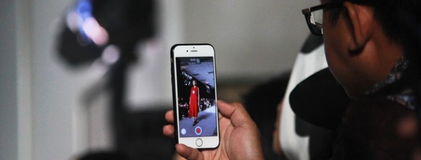 Photograph of person using mobile phone to take a picture of someone modelling clothing